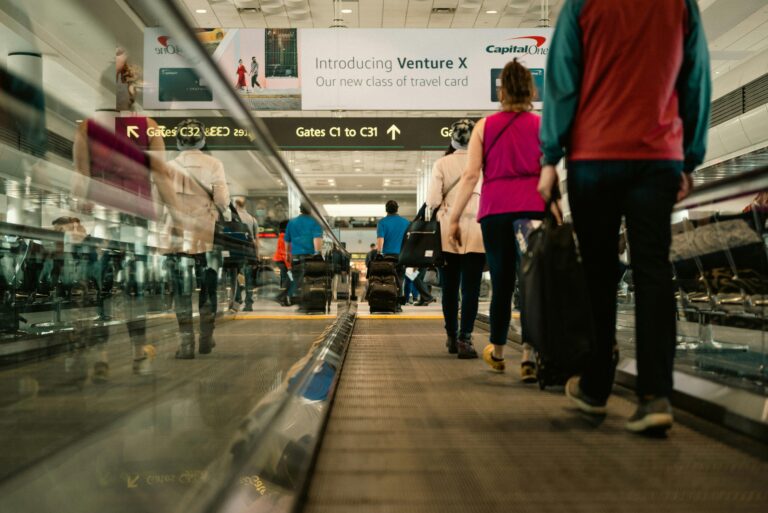 Passengers walking on a moving walkway in a busy airport terminal with signs for gates.